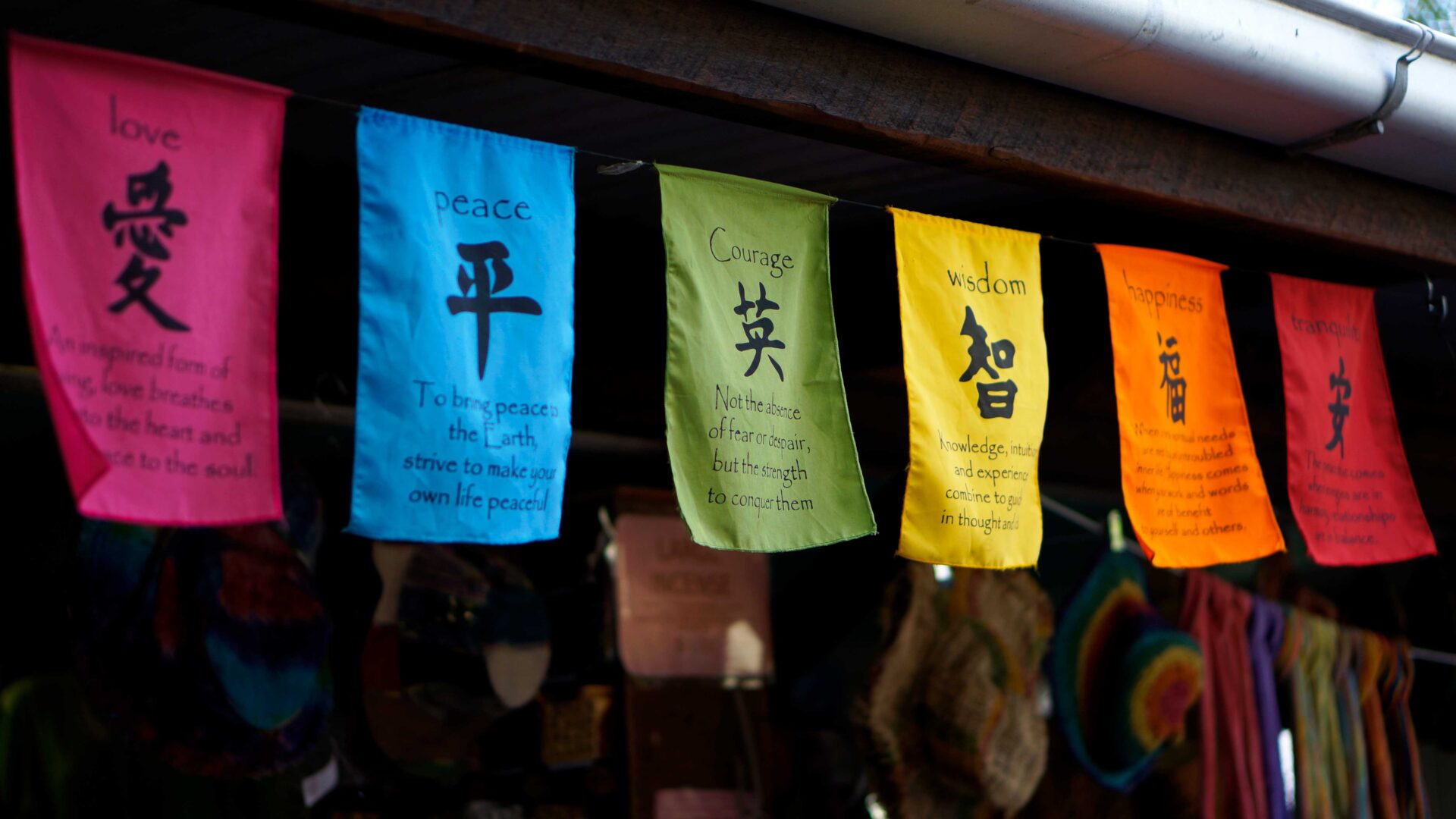 漢字が書かれた色とりどりの旗。愛・平・英・智・福・安の文字と英語の説明が並ぶ土産物屋の軒先