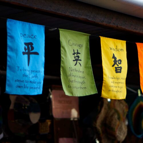 漢字が書かれた色とりどりの旗。愛・平・英・智・福・安の文字と英語の説明が並ぶ土産物屋の軒先
